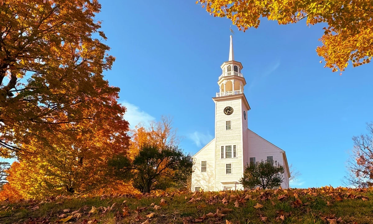 A white wooden church sits among fall foliage in New England