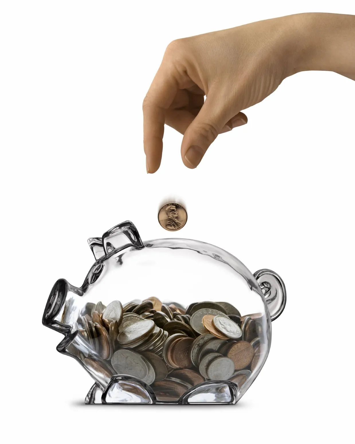 A hand dropping a coin into a clear glass piggy bank
