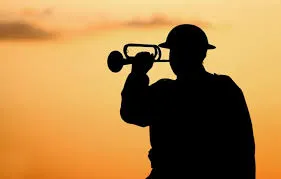 The silhouette of a soldier playing a bugle in front of a orange sky.