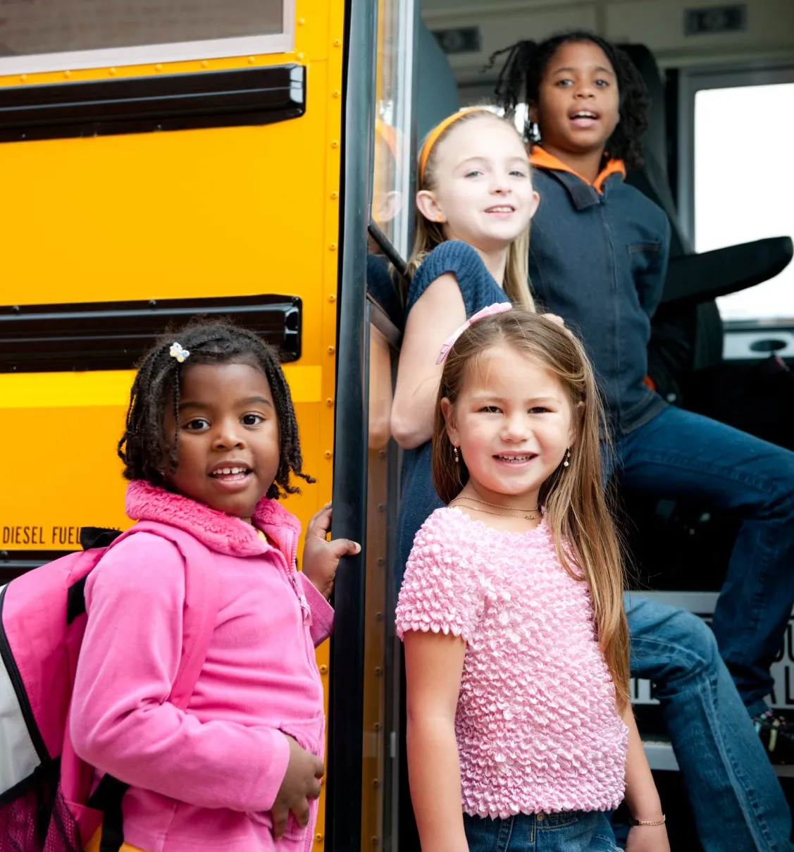A group of childre looking back at the camera boards a school bus.