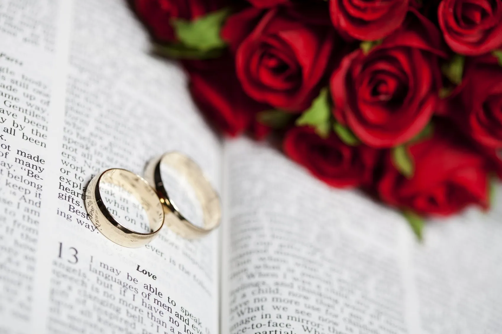 An open bible with a bouquet of roses and a pair of wedding rings resting on its pages.