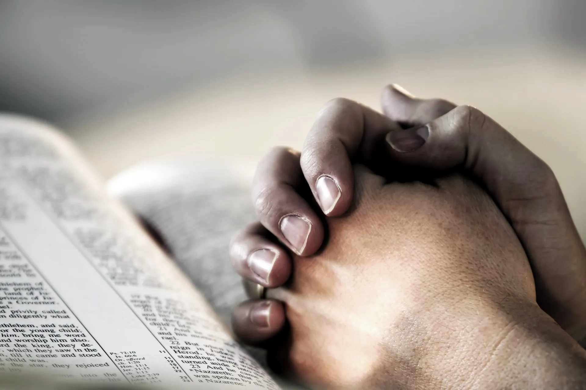 Interlaced hands over an open bible.