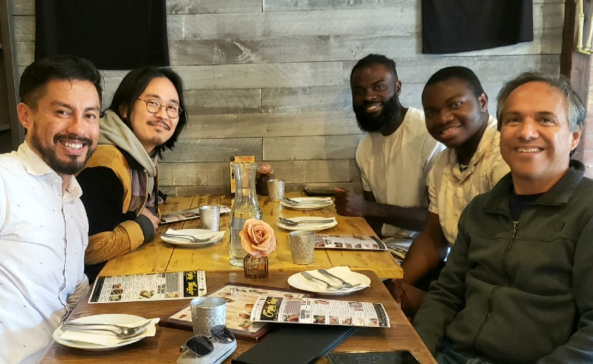 A group of five people sitting around a restaurant table posing and smiling for a photo