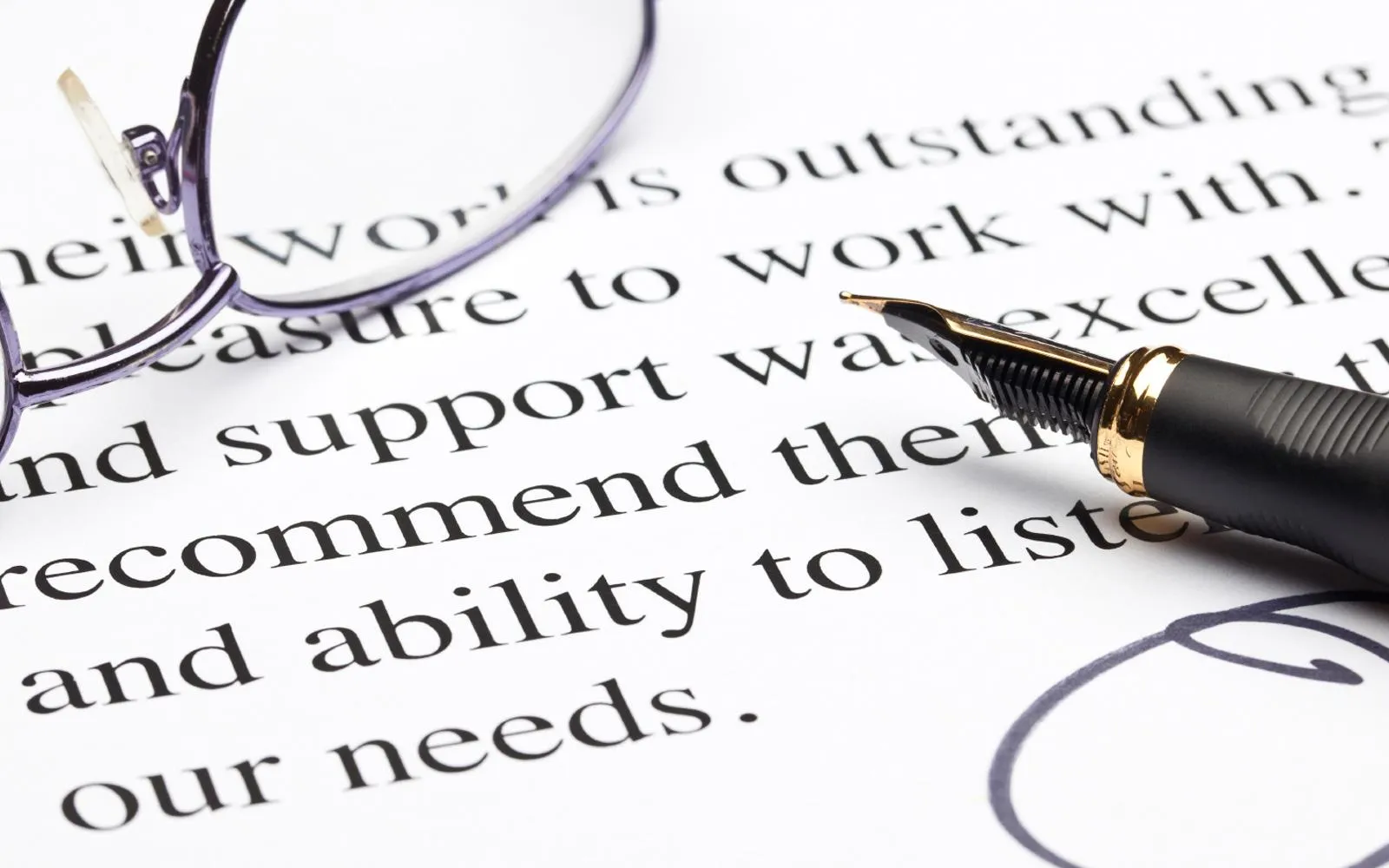 A closeup of a piece of paper with words printed on it, with a quill tip pen and pair of glasses resting on top of it.