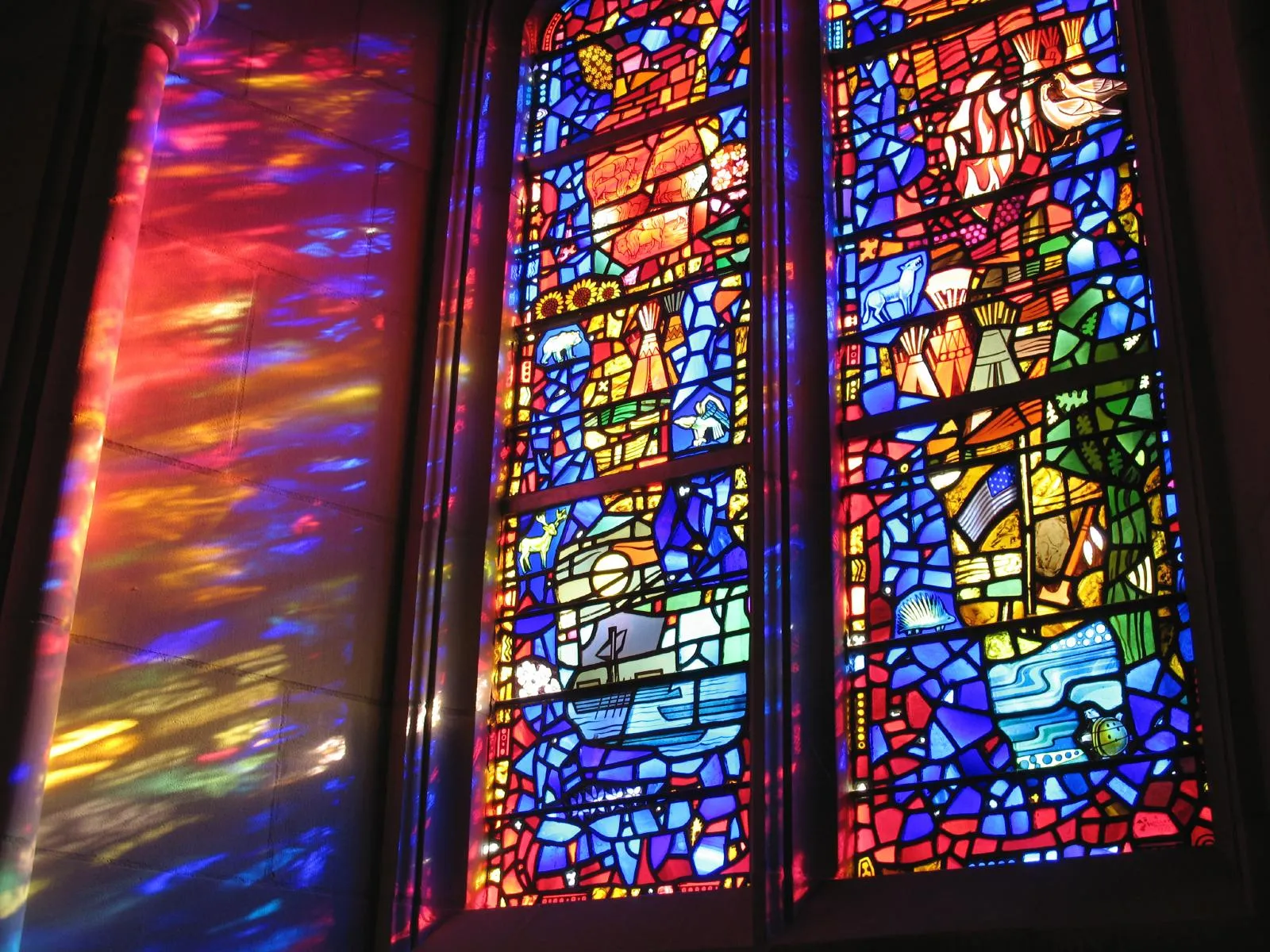 Two large stained glass windows reflecting their colors onto a wall.