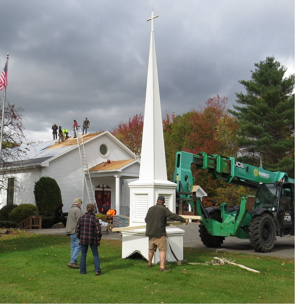 The spire of a church sits on the ground as a construction crew prepares to raise it to the rooftop