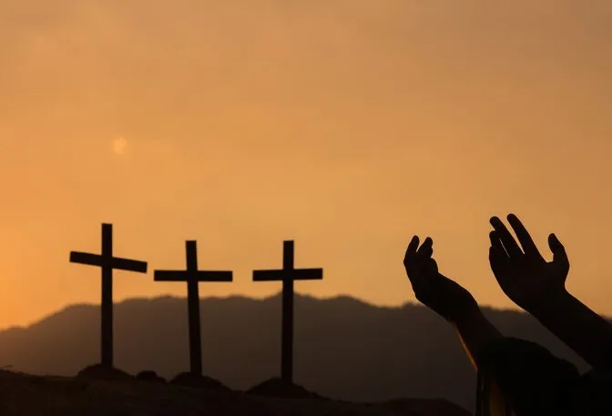 A pair of hands uplifted with three crosses in the background
