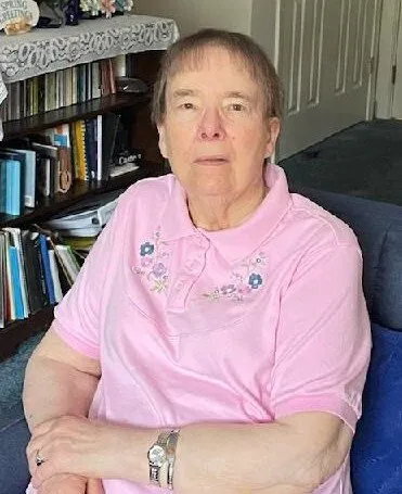 Photo of an older woman facing the camera, sitting in a chair.