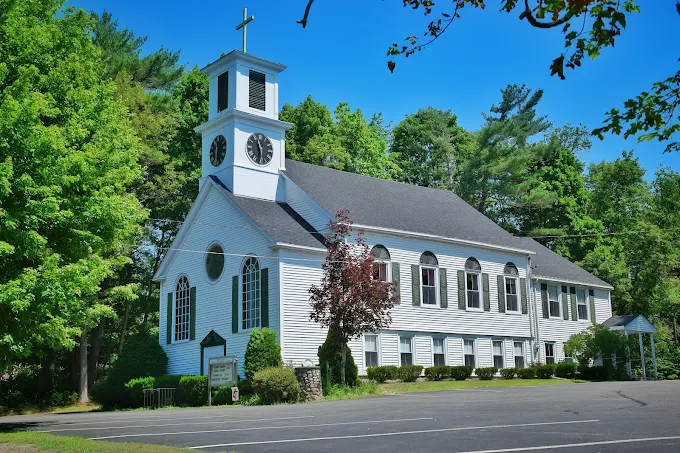 An outdoor photo of United Methodist Church Bryantville, a white church with shutters surrounded by green trees