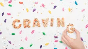 A white surface covered with sprinkles and cookies spilling the word "Craving", with a hand taking the "G" cookie.