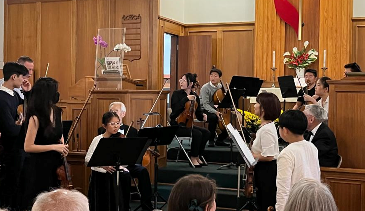 A church holding a small concert with young adults playing violins and other string instruments