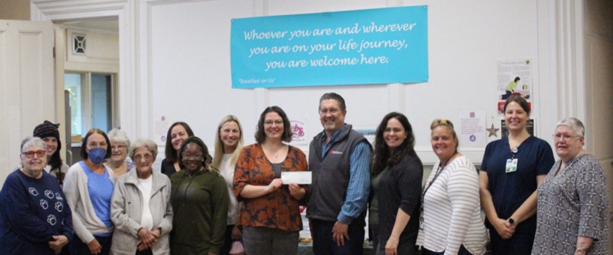 a group of people standing in front of a white wall with a blue poster holding a check