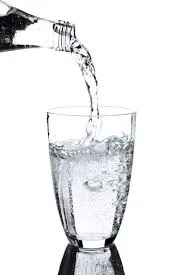 Water being poured into a clear glass from a glass bottle.