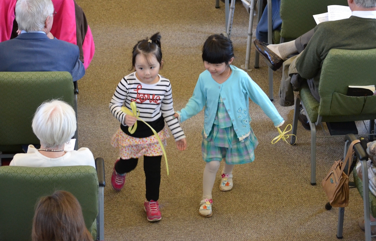 Two children walk down the aisle of a church holding palms in the shape of a cross