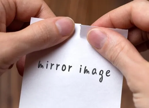 Hands tearing a small piece of paper with the words "Mirror Image" on it