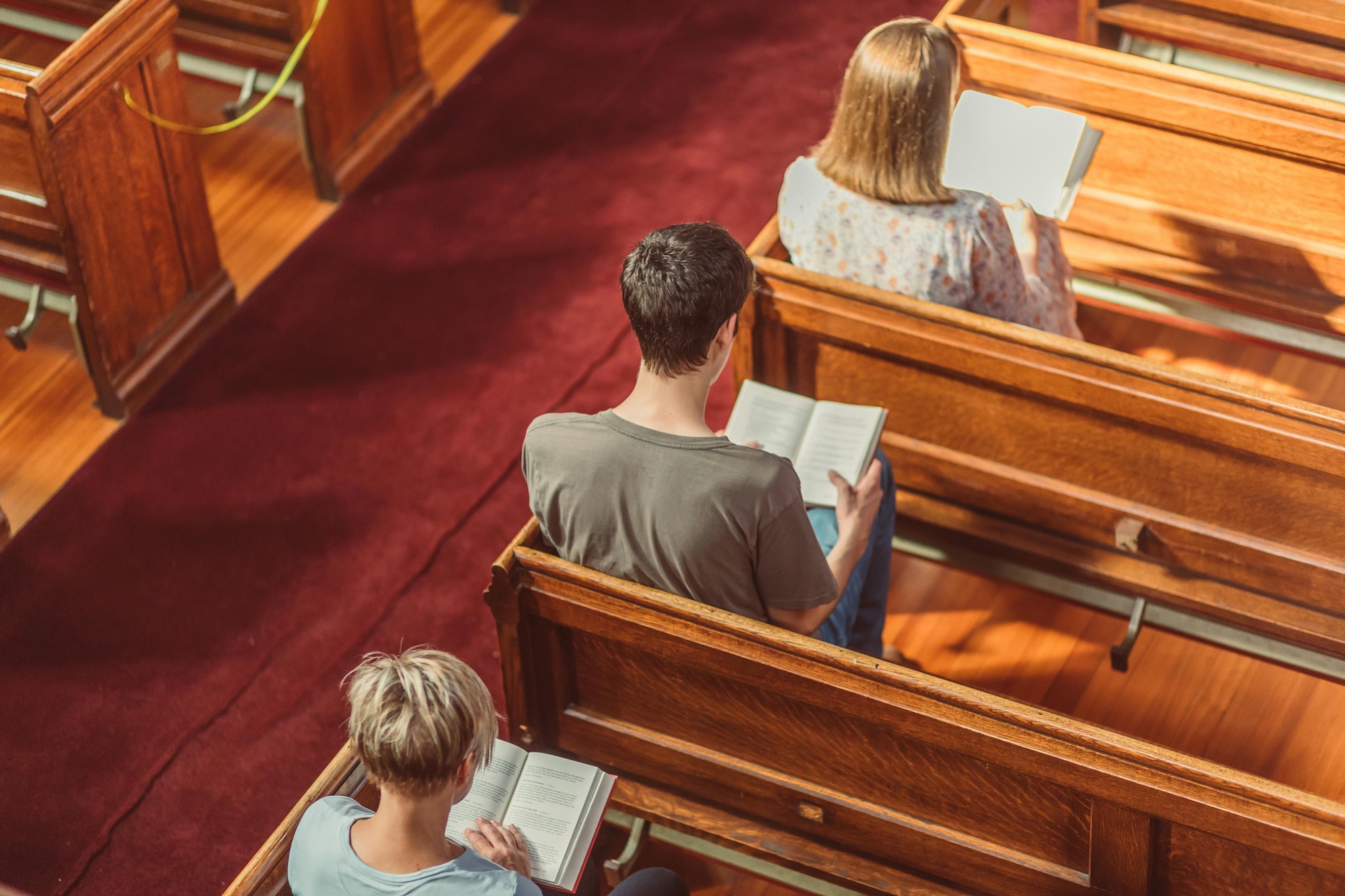Three individuals sit in pews, reading from hymnals in a Methodist Church