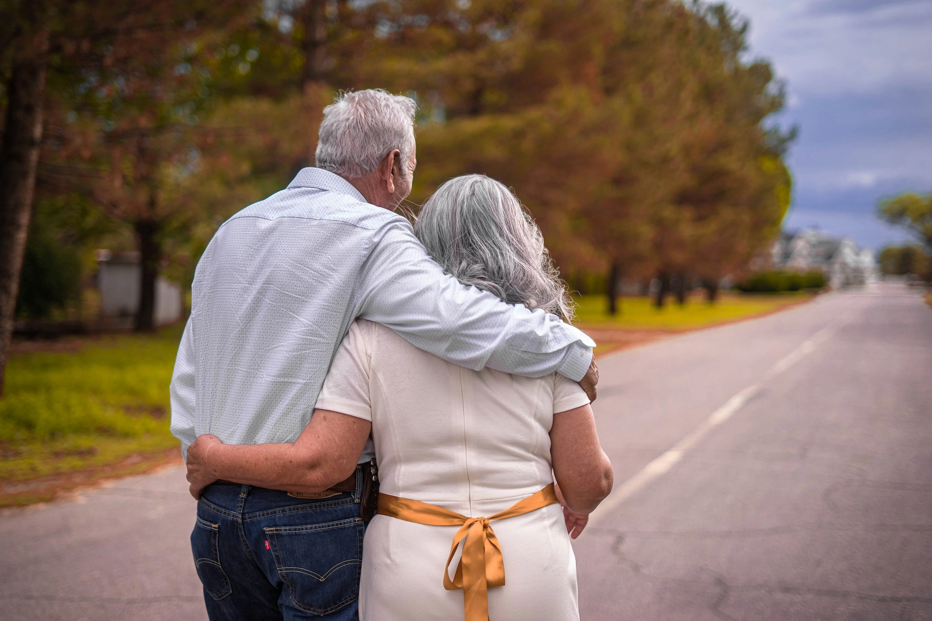 An older couple wrap their arms around each other as they walk down a rural street