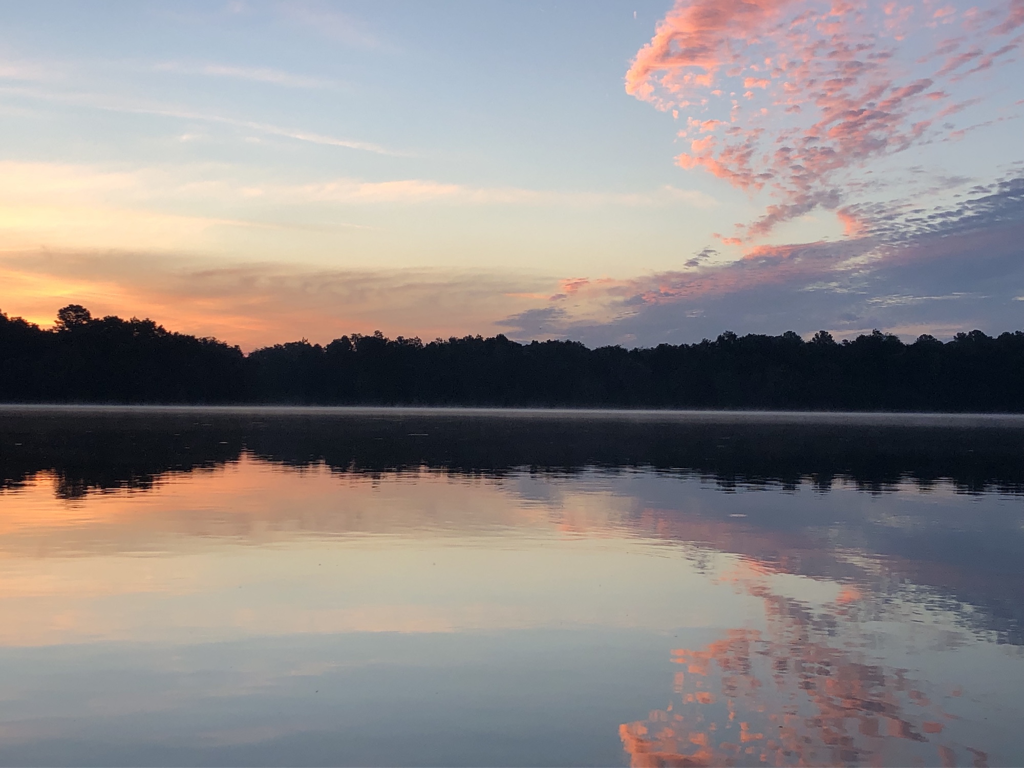 A sunset casts vibrant colors across the sky and across the reflections of a lake